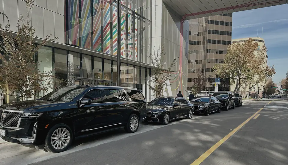 A black Cadillac Escalade and black Mercedes S-Class sedans parked along a city street