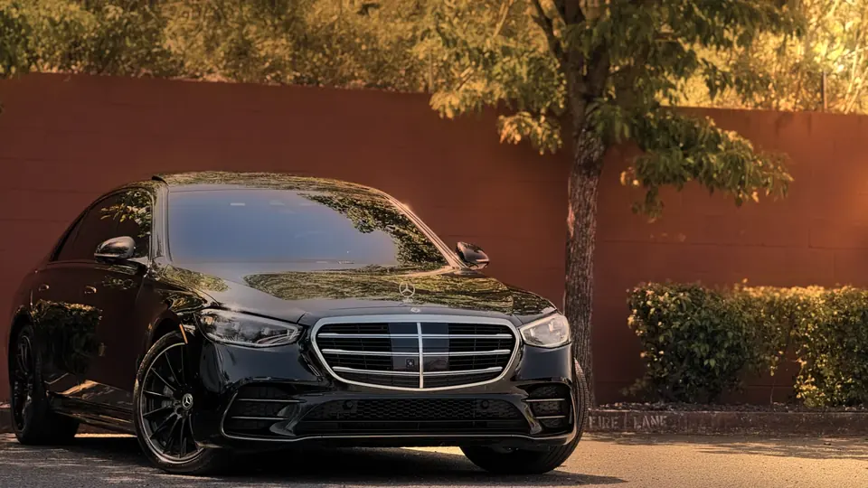 A black Mercedes S-Class in front of a red wall, a tree beside it