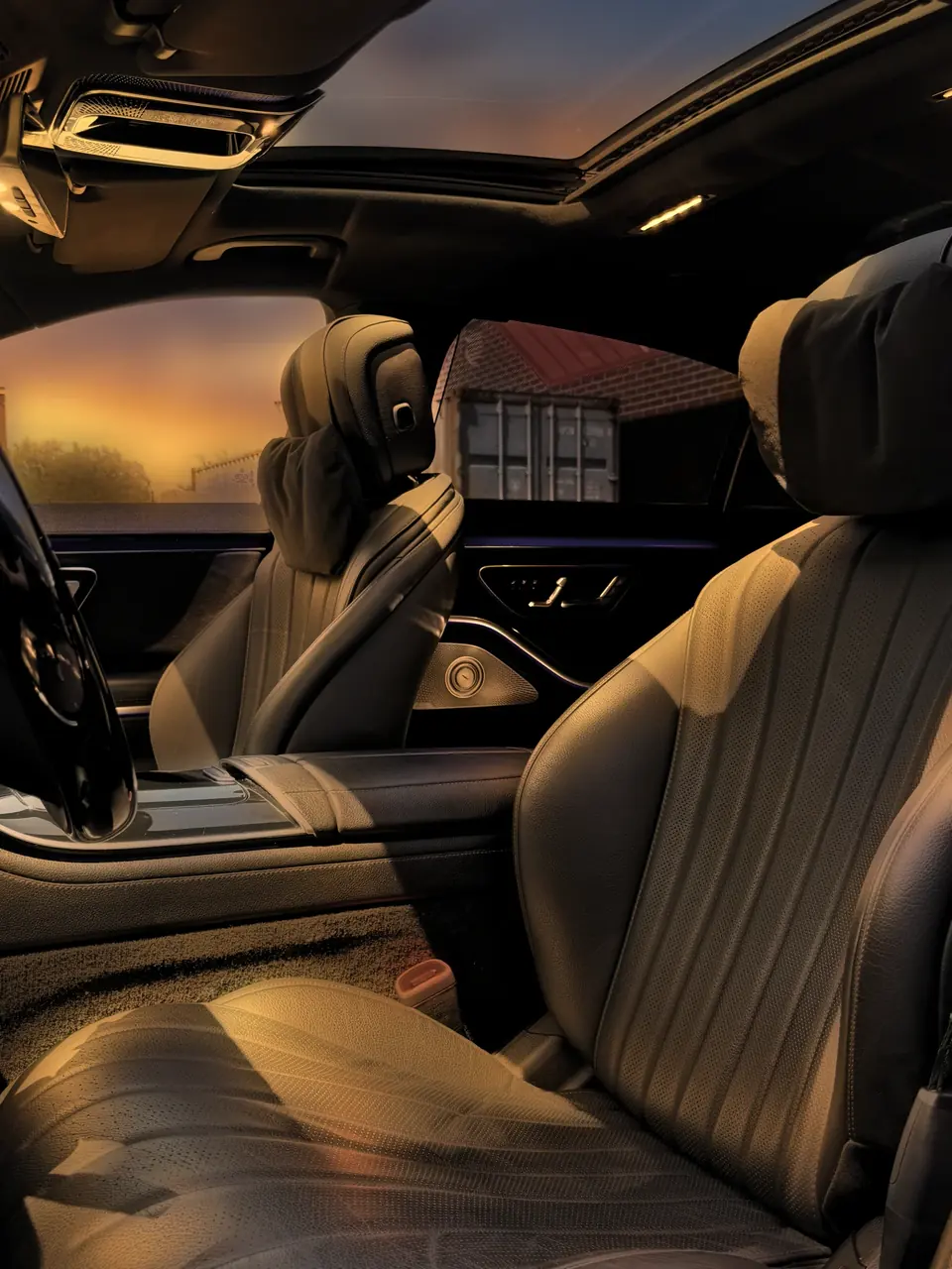 The front seats of a Mercedes S-Class beneath an open sunroof at sunset