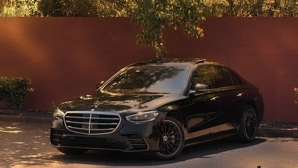 A black Mercedes S-Class parked by a red wall in afternoon light
