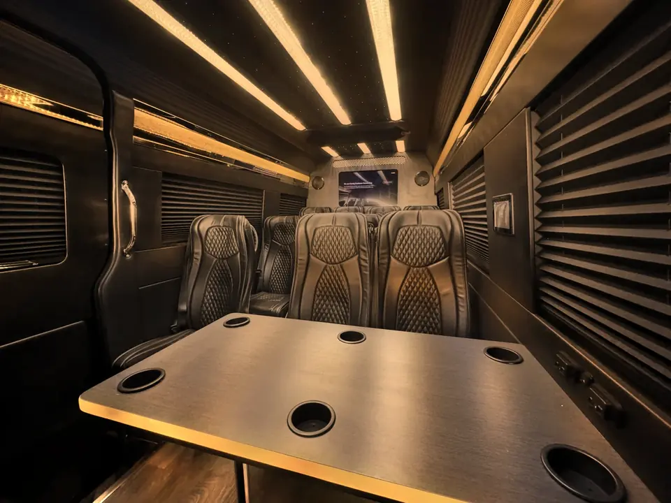 Leather seats facing a table inside a Mercedes Sprinter van, lights along the ceiling